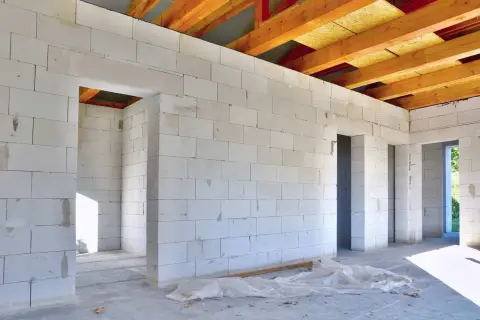 Budowa domu z białych bloczków z betonu komórkowego, widoczne drewniane belki stropowe.